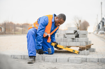 African american master in gloves lays paving stones in layers. Garden brick pathway paving by...