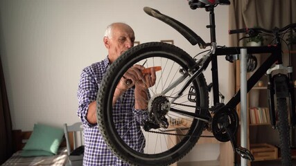 Grandpa in plaid shirt repairing bicycle, attaching reflector to wheel using screwdriver. Concept of bike safety, home tuning, and transport maintenance hobby.