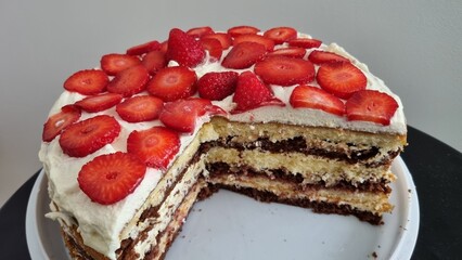 cake with cherries. Cake with white and chocolate layers and sliced strawberries and white cream on the black table, white background. 