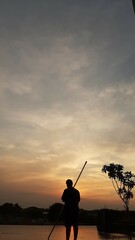 Silhouette of a Person with a Stick at Sunset Sky with Clouds and Tree.