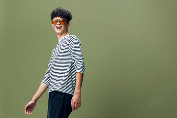 smiling man wearing sunglasses and striped shirt stands against green background with casual pose...