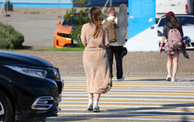 A woman in a tan dress is walking across a crosswalk