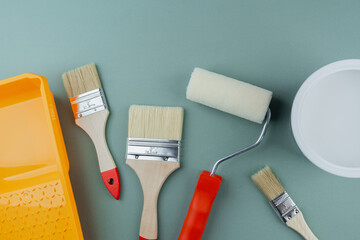 Scattered paint tools with roller, brushes, tray and bucket on green background for interior...