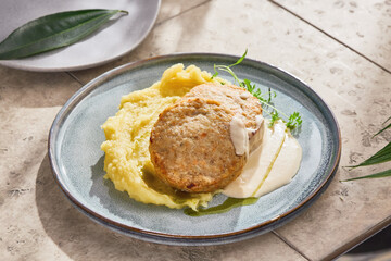 Mashed potatoes and fish patties with creamy sauce, bright lighting, angled composition