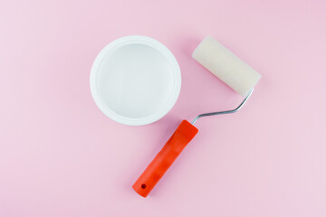 Open white paint bucket and roller on pink background for DIY painting supplies and preparation...