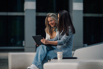 Two businesswomen using tablet and smiling outdoors in urban setting