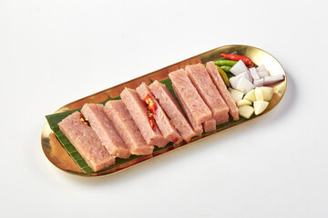 Fermented pork slices served on golden tray with banana leaf, garnished with fresh chili, garlic,...
