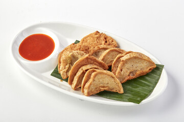 Crispy fried steamed pork rolls served on white plate with banana leaf base and side of red chili dipping sauce, offering savory and spicy flavor combination