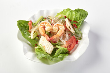 Vibrant plate of spicy kelp noodle salad with shrimp, squid, fresh lettuce, tomato, and herbs, offering refreshing and zesty flavor