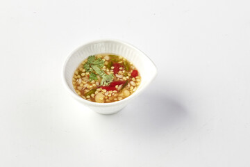 Small white ceramic bowl filled with spicy Thai chili sauce, featuring red chili slices, garlic, lime juice, and cilantro, placed on clean white background