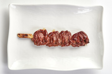 Grilled chicken hearts on skewer served on white rectangular plate, showcasing glossy, caramelized...