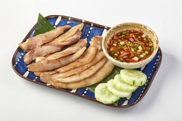 Grilled pork neck slices served with spicy dipping sauce, garnished with fresh cucumber slices on blue ceramic plate, showcasing traditional and flavorful Thai dish