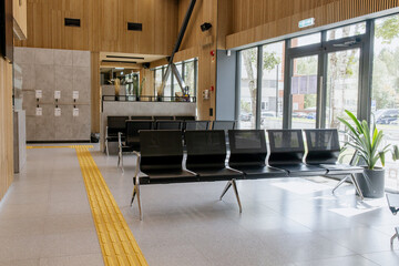 Empty waiting area in a public building, black metal benches, wooden slat walls, glass doors,...