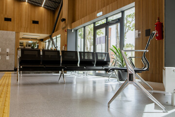 Empty waiting area in a public building, black metal benches, wooden slat walls, glass doors,...