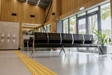 Empty waiting area in a public building, black metal benches, wooden slat walls, glass doors,...