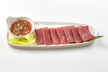 Freshly sliced raw beef served with spicy dipping sauce, garnished with lettuce and shredded vegetables on white plate, creating vibrant and appetizing presentation