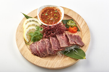 Thinly sliced raw beef served on wooden plate with fresh herbs, lemon slices, shredded vegetables, and spicy dipping sauce, creating vibrant and appetizing presentation