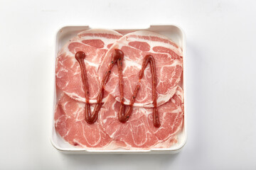 Thinly sliced raw pork arranged in white tray with drizzle of sauce on top, perfect for hot pot or...
