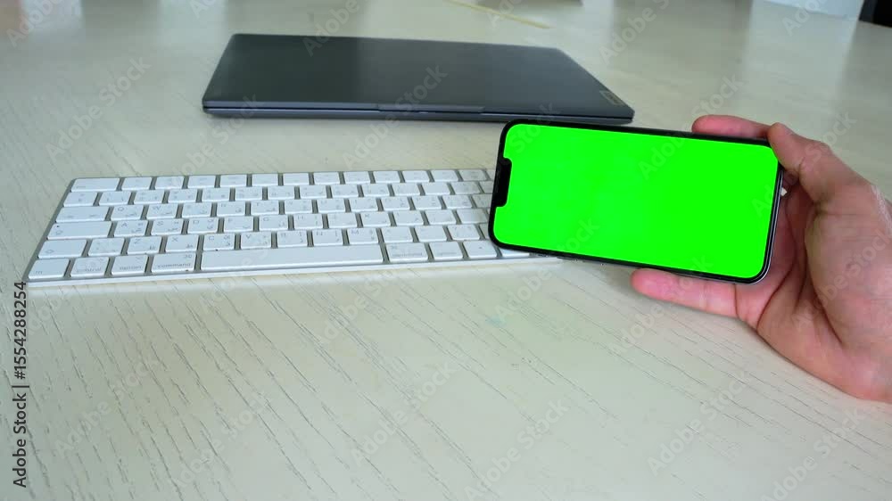 Poster Horizontal smartphone with green screen held above bilingual keyboard. Perfect for app demos, UI templates, and screen replacement in tech content.