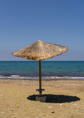 Straw umbrella casting shadow on sandy beach in southern Cyprus, with view of blue Mediterranean Sea. Peaceful summer scene with copy space, ideal for travel and vacation themes.