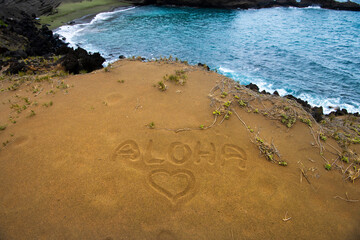 The word “ALOHA” with a heart symbol drawn in the sand at Green Sand Beach on the Big Island of...
