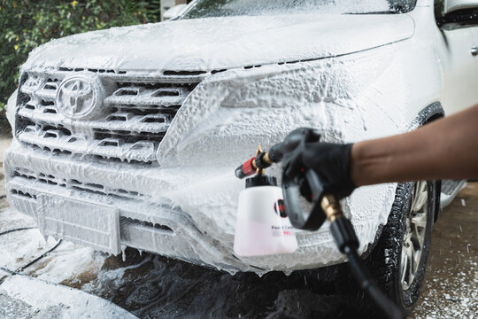 Bangkok, Thailand -June27,2025: professional hand applies thick snow foam to a modern white SUV during a thorough car wash and detailing session. The rich, clinging foam lifts dirt and grime.