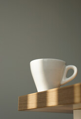 Close up white coffee cup on wooden table under morning window light on clean grey wall background in vertical.