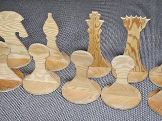 Row of wooden chess pieces are lined up on a carpet. The pieces are all different sizes and shapes