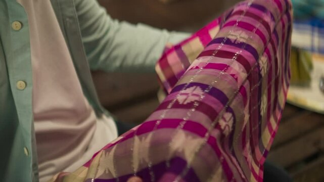 Close-Up of Hands Inspecting a Silk Sarong &ndash; Traditional Fabric Appreciation in Indonesian Culture