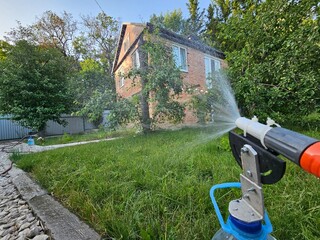 Hose is spraying water on a lawn. The hose is attached to a water source. The water is coming out...