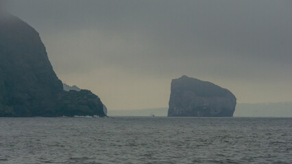Dramatic coastal landscape featuring rugged cliffs and distant rock formations shrouded in mist,...