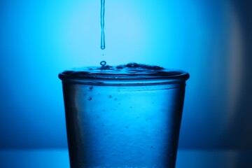 Fresh water in glass on blue gradient background, closeup. Backlit