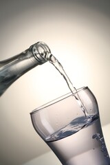 Pouring water from bottle into glass on gray gradient background, closeup