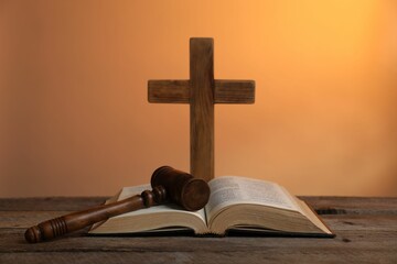 Judge's gavel, Bible and cross on wooden table against pale orange background, closeup