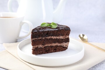 Piece of delicious chocolate cake with mint and spoon on grey table, closeup