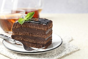 Piece of chocolate cake served with mint, fork and tea on white table, closeup. Space for text