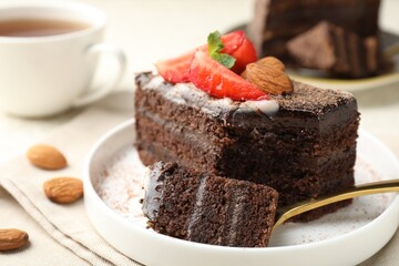 Piece of delicious chocolate cake with strawberry, almonds and tea on table, closeup