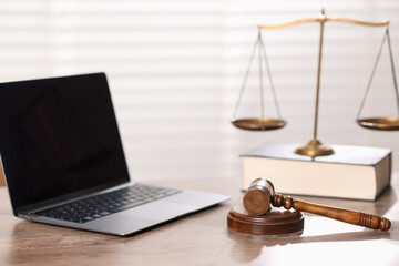 Judge. Laptop, gavel, scales and book on wooden table in office, selective focus