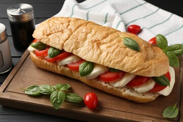 Tasty sandwich with mozzarella cheese, tomatoes and basil on black wooden table, closeup