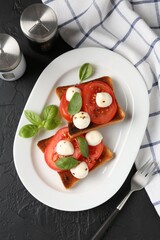 Tasty sandwiches with mozzarella cheese, tomatoes, basil and fork on dark textured table, flat lay