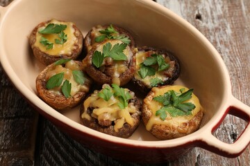 Delicious stuffed mushrooms with melted cheese and parsley in baking dish on color wooden table,...