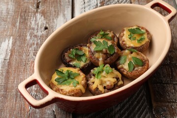 Delicious stuffed mushrooms with melted cheese and parsley in baking dish on color wooden table,...