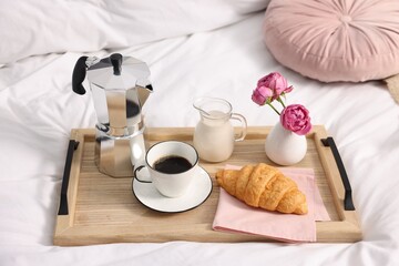 Tray with delicious breakfast and flowers on bed indoors, closeup