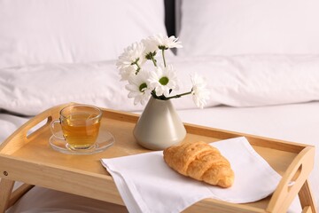 Tray with delicious breakfast and flowers on bed indoors, closeup