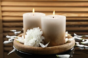 Burning candles and beautiful flowers on wet black mirror surface, closeup