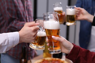 Friends clinking glasses of beer indoors, closeup