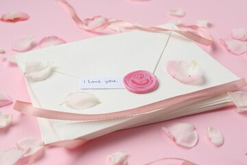 Stack of letters with phrase I Love You and petals on pink background, closeup