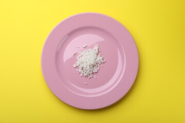 Plate with cooked rice on yellow background, top view
