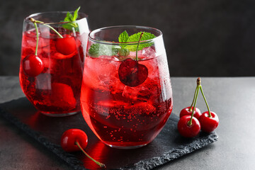 Tasty cherry soda with ice cubes, berries and mint in glasses on grey table, closeup