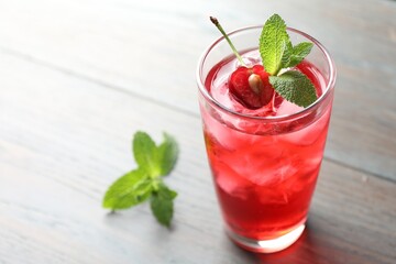 Tasty cherry soda water with ice cubes, berry and mint in glass on light table, closeup. Space for...